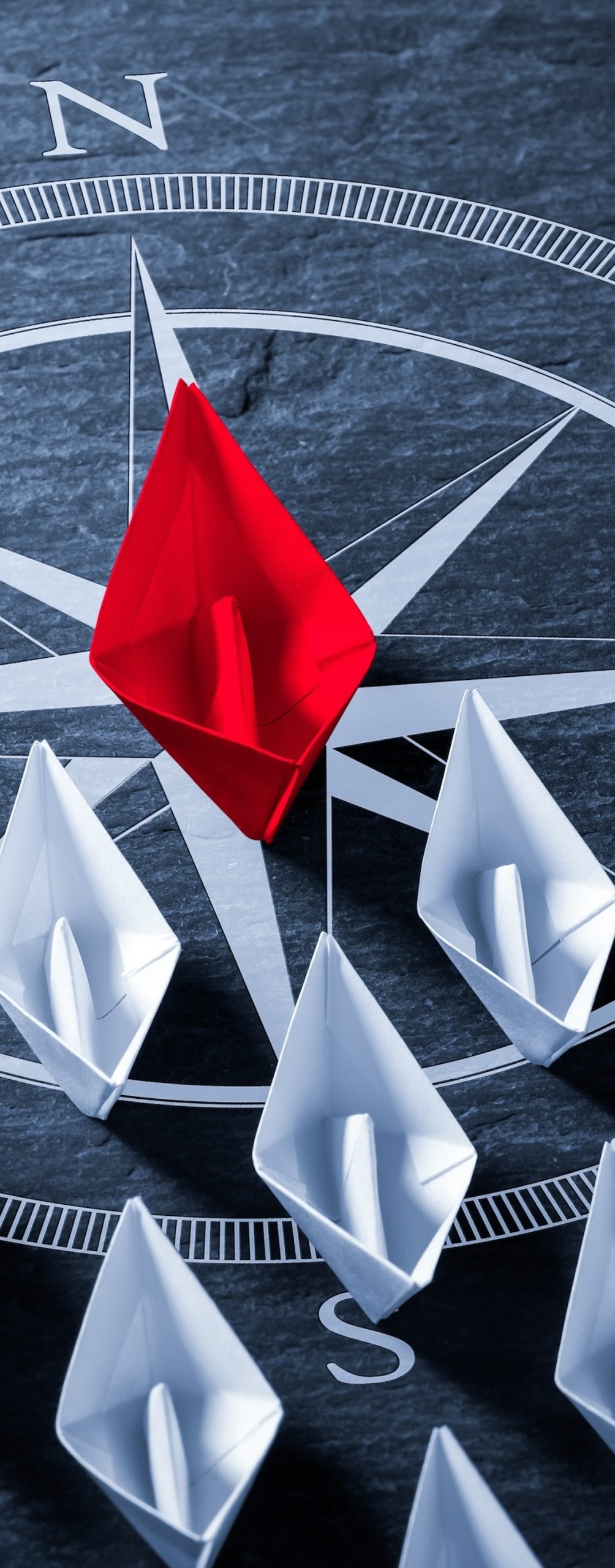 Red,Paper,Boat,On,Compass,Leading,A,Fleet,Of,Small
